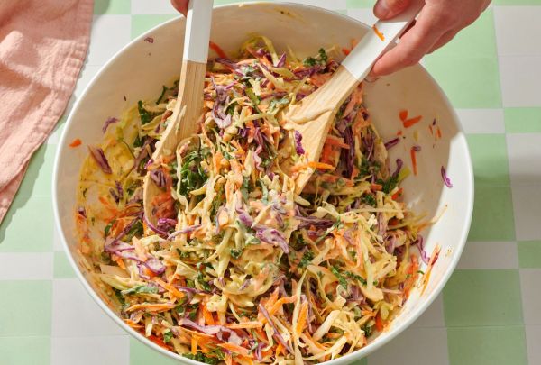 Hands mixing a slaw salad with wooden utensils in a large bowl Credit: Diana Christruga