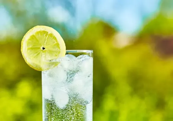 Sparkling water and lemon slice on glass with an ice, sunny day - narrow focus on middle of the glass