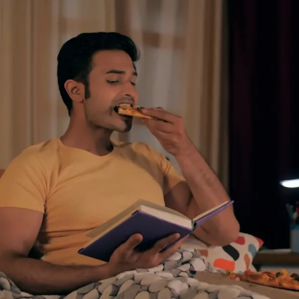 man eating pizza and reading book at home alone