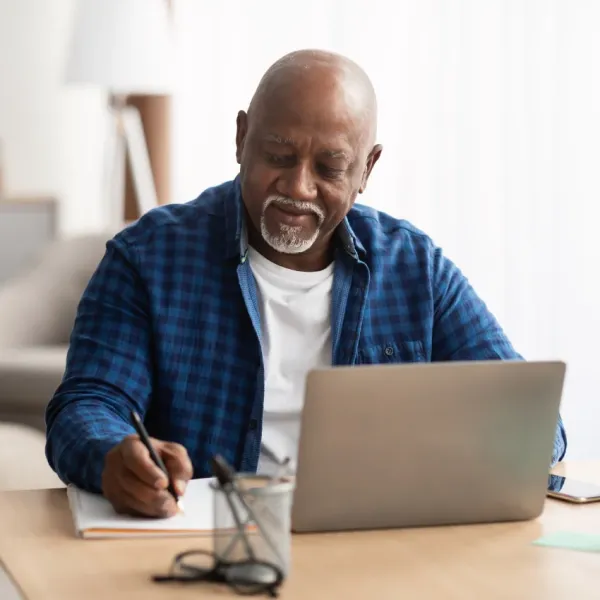man working on laptop and writing on pad