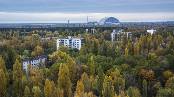 An ariel view showing apartment buildings amidst the forests in Chernobyl. In the background, the New Safe Confinement structure sitting over reactor 4 can be seen.