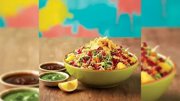 A vibrant green bowl filled with healthy sprouts chaat made of green moong sprouts, pomegranate seeds, grated carrots, and beetroot, topped with crunchy cornflakes, served with green chutney and a lemon wedge on a colorful background.