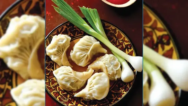 Five steamed veg momos on a decorative ceramic plate, garnished with fresh spring onions.