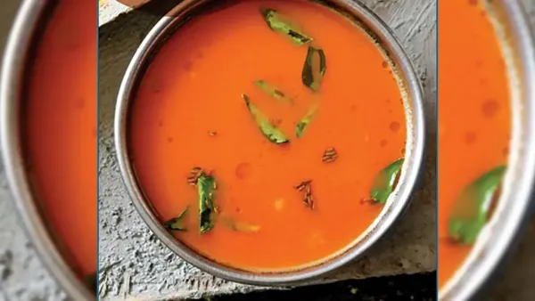 A top-down view of a small steel bowl filled with smooth orange chutney tomato, tempered with fresh curry leaves