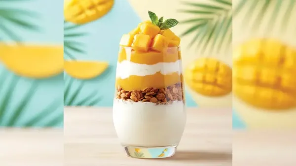 A layered glass of healthy mango parfait with yogurt, granola, and fresh mango puree, topped with juicy mango cubes and mint.