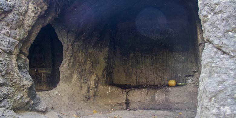 Suasana bagian dalam Gua Selomangleng yang dipenuhi relief kuno pada dinding batu andesit, serta terdapat perlengkapan ritual seperti dupa dan kelapa muda.