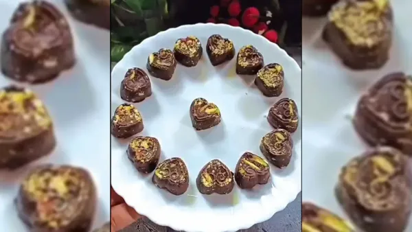 Heart-shaped homemade dark chocolates decorated with crushed pistachios, arranged in a circular pattern on a scalloped white plate.