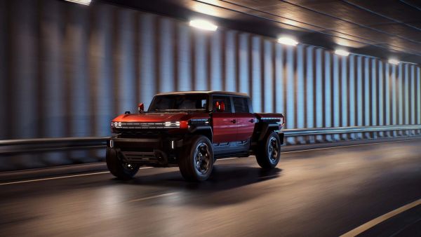 Red and black electric pickup truck driving in a tunnel with illuminated ribbed walls.