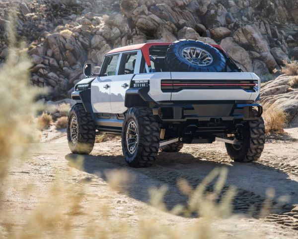 White and red off-road SUV with large tires parked on a dirt trail with rocky hills in the background.