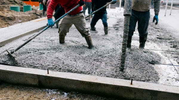 Several construction workers using tools to flatten freshly laid concrete
