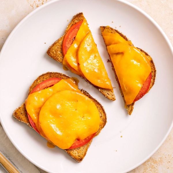 Two slices of toast with melted cheddar cheese and tomato on a white plate cut into halves Credit: Abbey Littlejohn