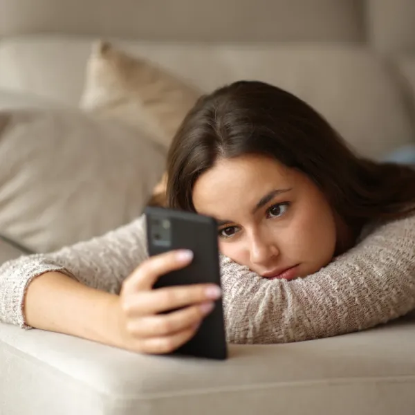 tired woman sitting on couch looking at her phone