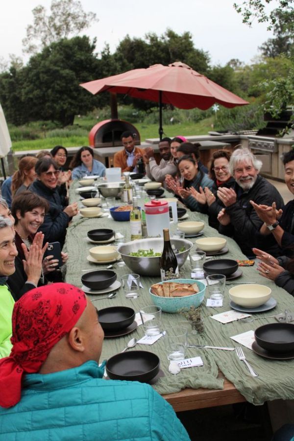 Guests seated at a long outdoor table sharing a communal meal Credit: Courtesy Photo