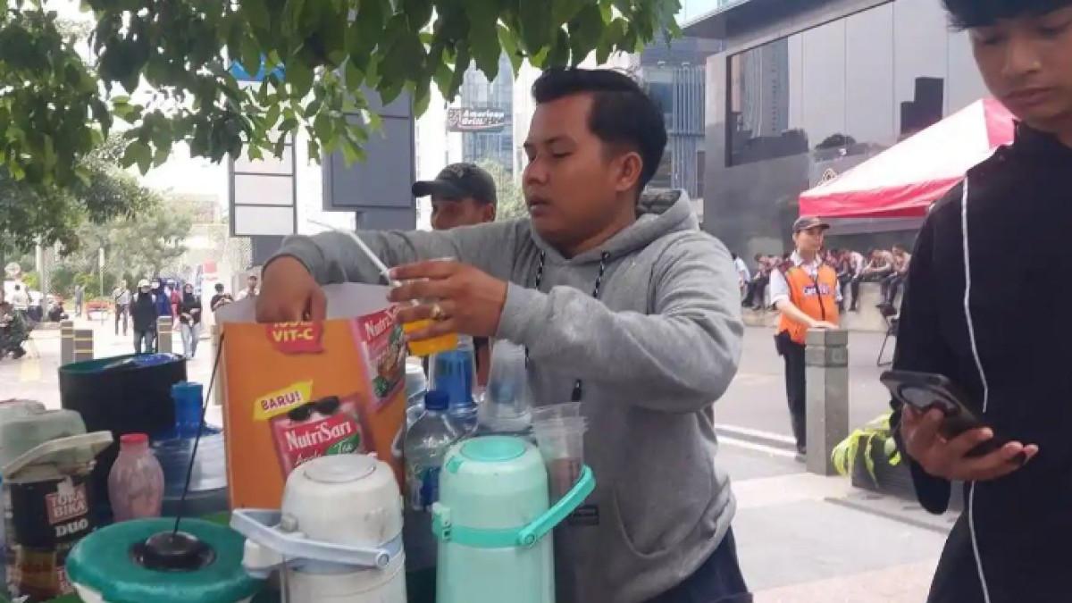 AKSI DEMO - Pedagang kopi keliling atau starling bernama Fathur (30) sedang sibuk mengaduk minuman es yang dipesan pembeli di gerobak sepeda sederhananya saat aksi demonstrasi di kawasan Bundaran HI, Jakarta, Senin (15/6/2026).