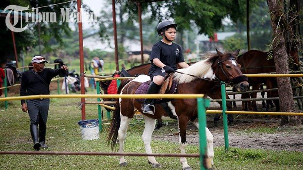 WISATA EDUKASI - Seorang anak menunggangi kuda ditemani pelatih di Taman Cadika Pramuka Jalan Karya Wisata, Kota Medan, Minggu (23/7). Pemko Medan akan segera merevitalisasi Taman Cadika Pramuka, dan berharap paska revitalisasi, dapat melahirkan atlet-atlet profesional.