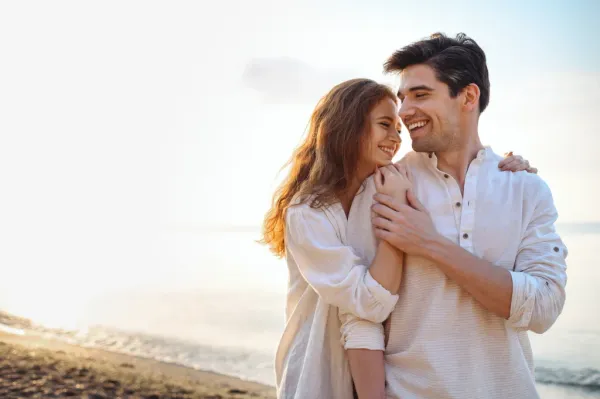 Smiling couple embracing on a beach with the ocean in the background.