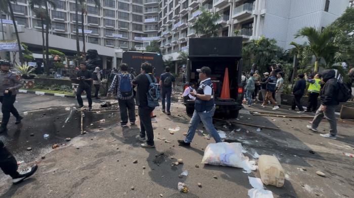Kondisi pasca-bentrokan di area pelataran Hotel Sultan, Jakarta Pusat pada Kamis (18/6/2026). Tampak batu dan puing-puing berserakan di jalanan, sementara aparat keamanan mulai merangsek masuk dan mengamankan area lobi utama hotel setelah berhasil memukul mundur massa.