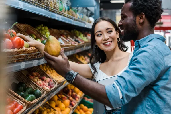 A happy Asian woman smiling at an African American man in a grocery store as they look at fruit.