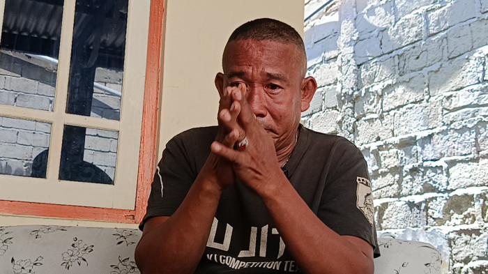 PASCA KEBAKARAN -- Yusran Yusuf meneteskan air mata saat menceritakan peristiwa kebakaran yang dialaminya, Rabu (17/6/2026). Sisa-sisa bangunan yang terbakar berhamburan di tanah. (Sumber Foto: TribunGorontalo.com/Jefri Potabuga)