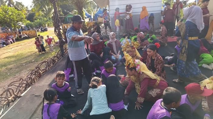 PERMAINAN LAWAS - Sejumlah murid Sekolah Dasar (SD) dipandu oleh Tetua Adat sekaligus Dukun Kampung Desa Lilangan, Syahiril atau Kik Kun (63), saat mempraktikkan permainan tradisional Belitong di atas panggung Festival Seni Budaya Desa Lilangan, Kecamatan Gantung, Belitung Timur, Selasa (23/6/2026). Lewat tiga permainan legendaris yaitu Pong Pong Along, Jajak Setunju, dan Sapu Sapu Rengit, generasi muda diajak untuk kembali melatih kekompakan, kejujuran, dan sportivitas sekaligus mengalihkan ketergantungan dari gawai.