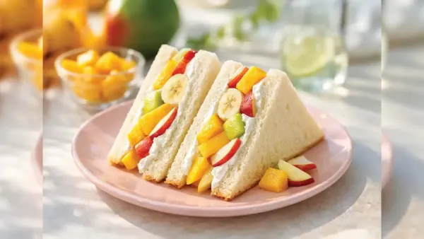 Two triangular fresh fruit cream sandwiches packed with sliced mango, banana, kiwi, and apples on a pink plate.