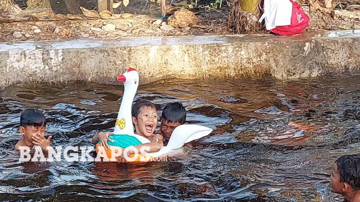 BERMAIN AIR – Sejumlah anak-anak ketika bermain air di Pemandian Irigasi Viral Aik Item Desa Rias, Jumat (26/6/2026).  Pemandian tersebut kini mulai ramai diserbu pengunjung selama satu bulan terakhir. (Bangkapos.com/Cepi Marlianto)