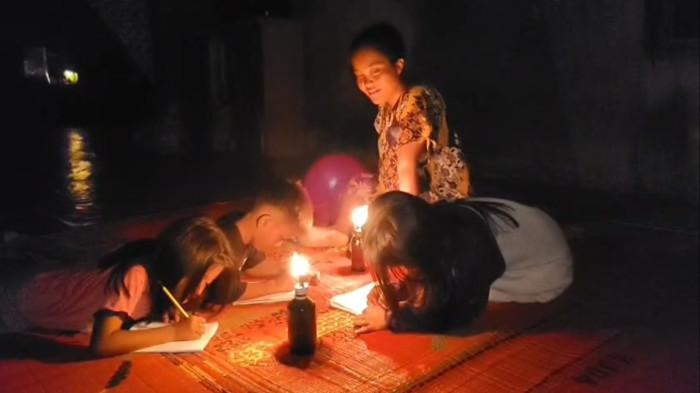 Tiga orang anak mengerjakan tugas sekolah ditemani lentera karena belum adanya aliran listrik masuk ke perkampungan dusun delapan, Desa Pertahanan, Sei Kepayang, Kabupaten Asahan.