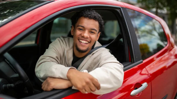 A driver smiling and leaning out of a car window.