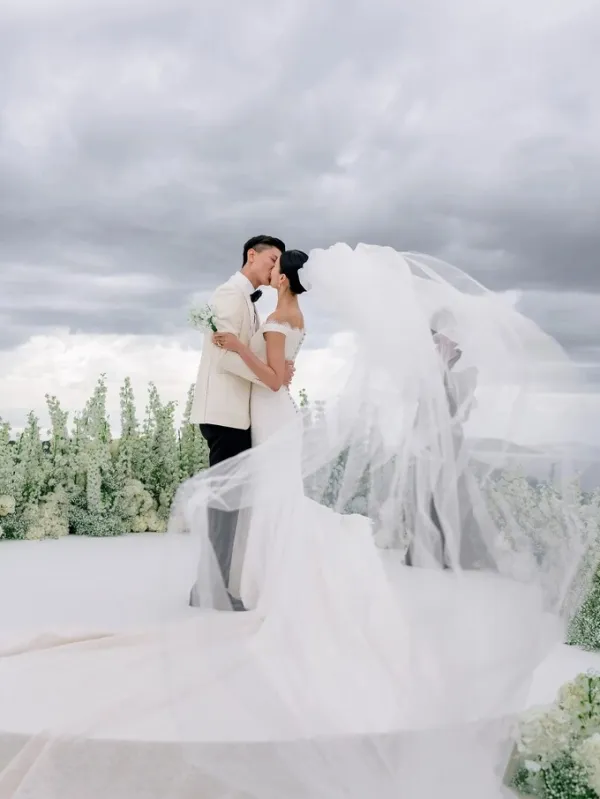 On the main wedding day, Liu started in a 1996 archival Chanel haute couture dress and coat with an embroidered bow and then changed into a custom Chanel wedding gown with a mermaid silhouette, off-shoulder neckline, long train, the houses signature back buttons and camellia lace, Chanels floral emblem since its founder Gabrielle Chanel adopted the flower in the 1920s. A long minimal veil completed the look.