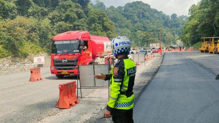 PERLAMBATAN ARUS LALIN - Petugas Satlantas Polres Padang Panjang mengatur arus lalu lintas dengan sistem buka tutup di Jalur Lembah Anai, Kabupaten Tanah Datar, Minggu (28/6/2026). Rekayasa lalu lintas diberlakukan akibat pekerjaan pengaspalan di dua titik, yakni di Kilometer 63 dan kawasan Jembatan Kembar, sehingga menyebabkan antrean kendaraan dari arah Padang maupun Padang Panjang.