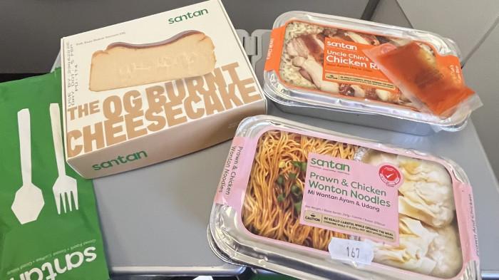 Aneka menu Santan AirAsia tersaji di atas meja penumpang dalam penerbangan langsung AK2354 rute Jakarta–Kota Bharu, Kamis (25/6/2026). Hidangan yang ditawarkan meliputi Uncle Chin's Chicken Rice, Prawn & Chicken Wonton Noodles, serta OG Burnt Cheesecake yang dapat dipesan melalui layanan Santan, merek makanan dan minuman milik AirAsia.