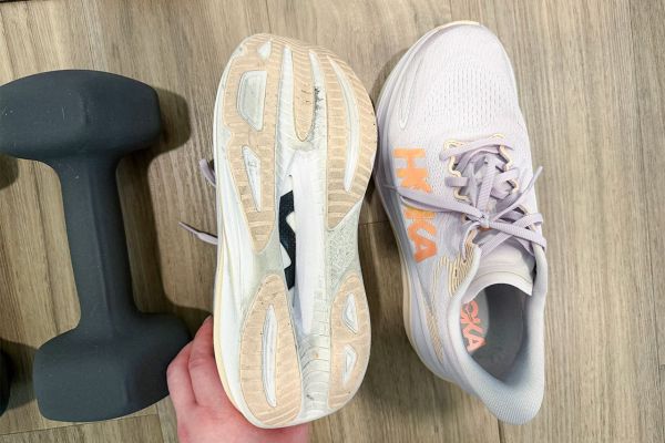 Running shoes with one showing the sole and the other in a top view beside a dumbbell on wooden floor Credit: EatingWell