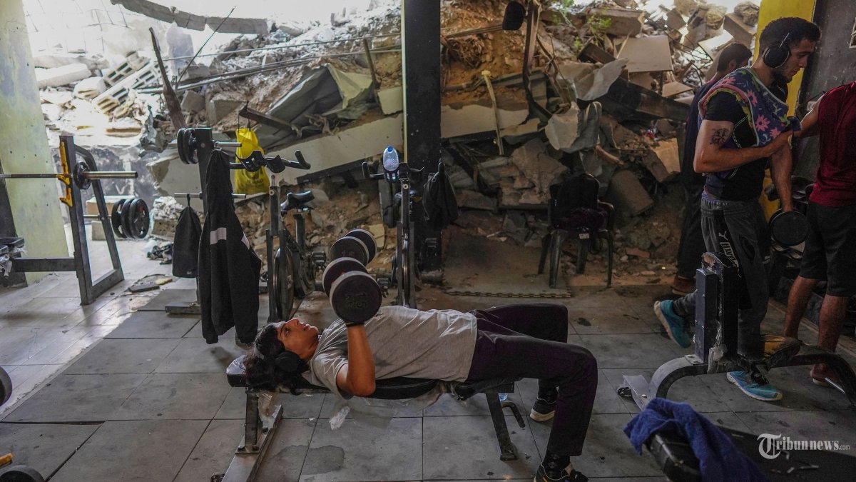 Warga Palestina berlatih angkat beban di pusat kebugaran yang rusak, yang baru-baru ini dibuka kembali di Khan Yunis di Jalur Gaza selatan pada 7 Agustus 2024 di tengah konflik yang sedang berlangsung antara Israel dan kelompok militan Hamas Palestina. (Photo by Bashar TALEB / AFP)