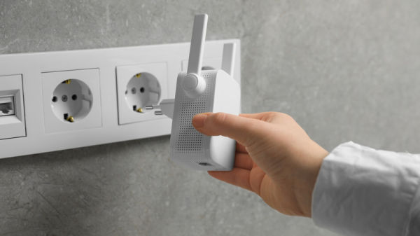A person's hand is about to plug in a white wi-fi extender in one of the multiple wall sockets available