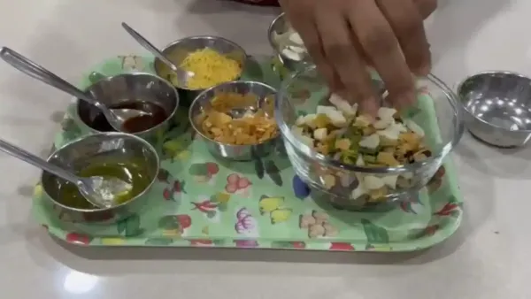 Close up of a hand preparing delicious black chickpea kala chana chaat with various flavorful Indian chutneys and spices.