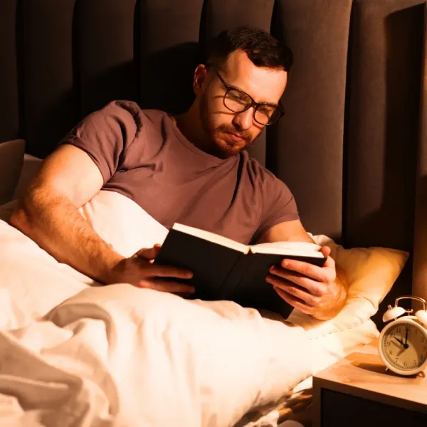 man reading a book in bed to relax himself before sleeping