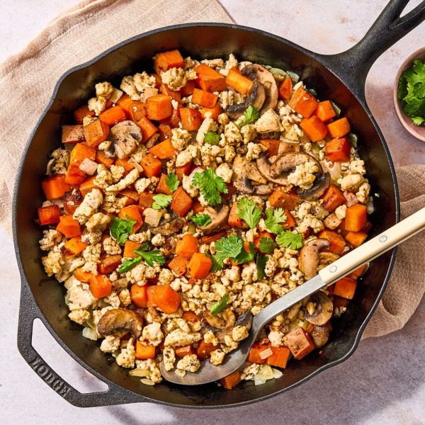 A skillet containing a mixed dish of ground turkey sweet potatoes and mushrooms garnished with cilantro with a serving spoon Credit: Ali Redmond