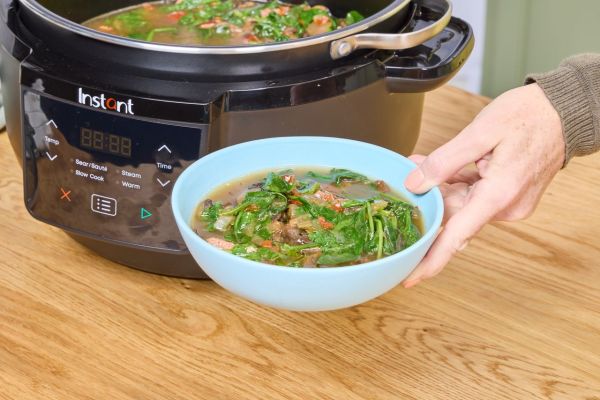A person holds a bowl of soup cooked in the Instant Superior Cooker 7.5QT Slow Cooker Credit: EatingWell