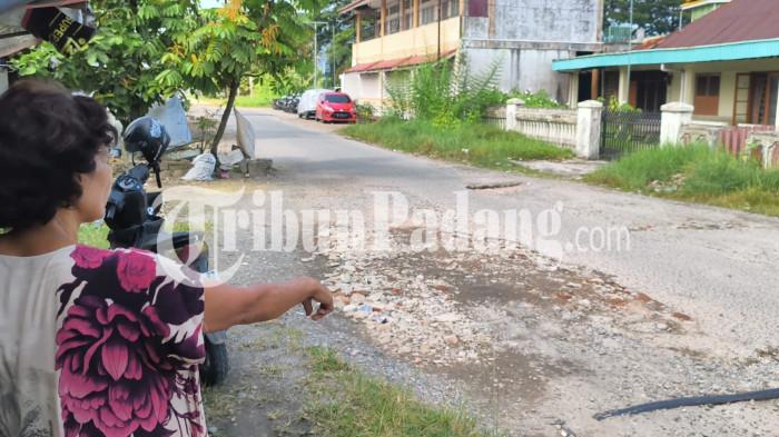 JALAN RUSAK- Warga, Asnimar saat menunjuk lokasi jalan rusak di Komplek PJKA, Kelurahan Sawahan Timur, Kota Padang, Jumat (17/7/2026). Warga sebut jalan rusak tak kunjung diperbaiki, warga inisiatif tambal dengan reruntuhan bangunan.