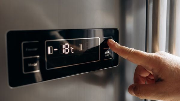 A person is using a digital temperature control panel on a refrigerator.
