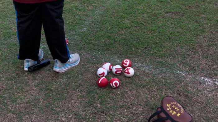 Bola-bola bernomor, stik pemukul, dan perlengkapan gateball tampak di atas lapangan berumput saat sesi latihan.