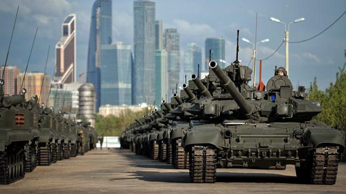 Deretan tank militer Rusia tampak berbaris rapi di jalanan dengan latar belakang gedung-gedung pencakar langit Moskow.