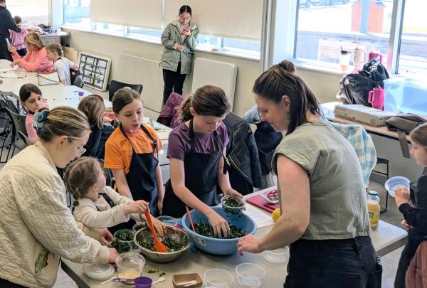 A group of children and an adult preparing food together at a classroom table emphasizing teamwork and handson learning Credit: Honest Weight Co-op.