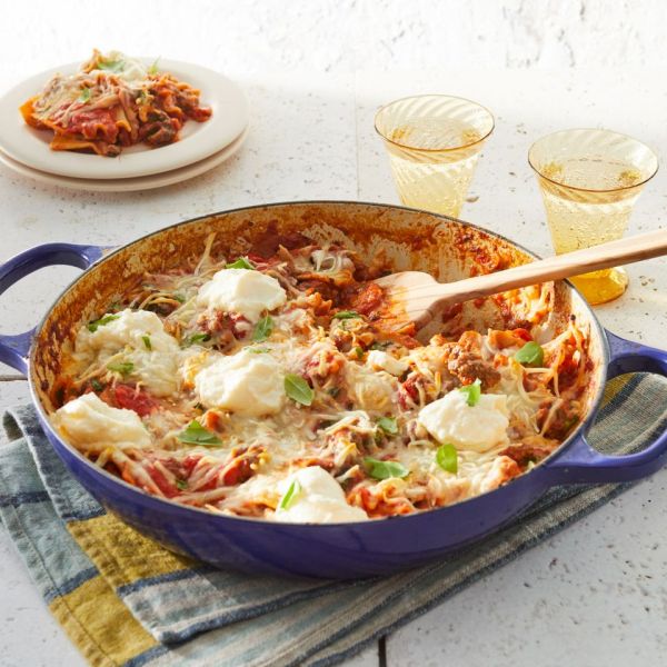 Skillet lasagna in a blue skillet, with two light yellow glasses in the background, as well as a plate with some of the lasagna on Credit: William Dickey