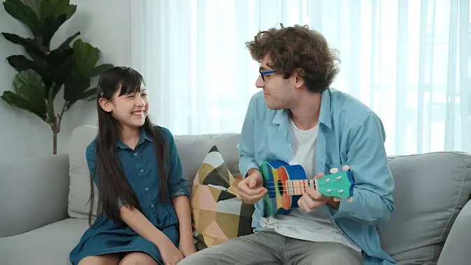 Seorang laki-laki bermain ukulele di hadapan seorang anak perempuan (Foto Dok: Freepik/Frolopiaton Palm).