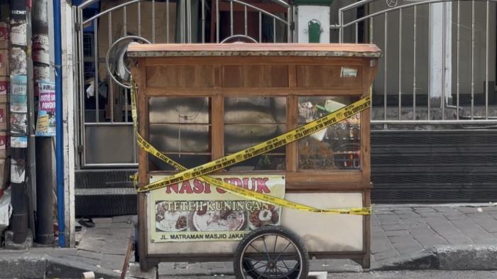 PEMICU BENTROKAN - Gerobak nasi uduk di Jalan Matraman Dalam, Menteng, Jakarta Pusat, tampak dipasangi garis polisi setelah mengalami kerusakan, Minggu (26/7/2026). Perusakan gerobak ini diduga kuat menjadi pemicu awal terjadinya bentrokan kelompok warga.
