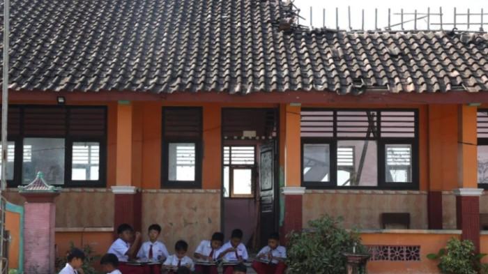 Siswa menyantap menu MBG dengan latar belakang ruang kelas mereka tanpa atap setelah ambruk berbulan-bulan di SD Negeri Tanggirejo, Kecamatan Tegowanu, Kabupaten Grobogan, Jawa Tengah, Selasa (21/7/2026).