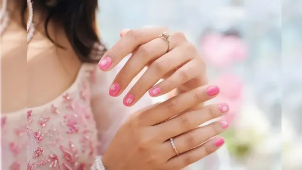 Woman displaying elegant bright pink manicured nails decorated with delicate white floral art and subtle rings setup.