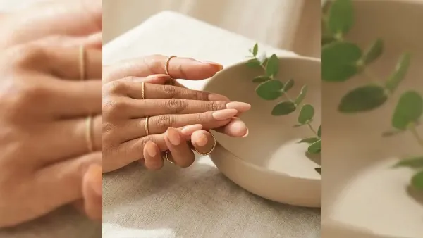 Woman showcasing minimal peach nude manicured nails adorned with thin gold rings beside a ceramic bowl setup.