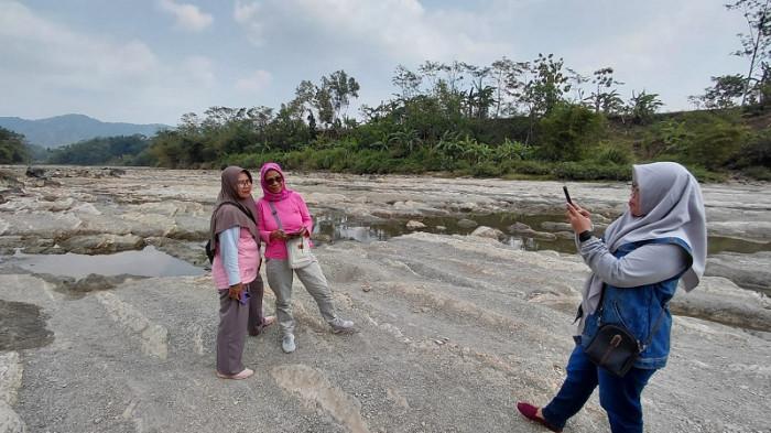 WISATA DADAKAN - Farida Zain dan kawannya saat berfoto di aliran Bendung Sungai Tajum di Desa Tipar Kidul, Kecamatan Ajibarang, Kabupaten Banyumas, Selasa (28/07/2026). Hamparan batu alam yang muncul akibat surutnya debit air, dipadu aliran sungai yang jernih dan udara sejuk, menghadirkan pengalaman wisata sederhana.